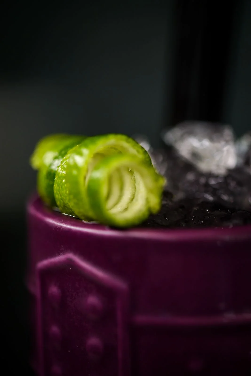 Lime peel spiral on a purple tiki mug with crushed ice, macro shot
