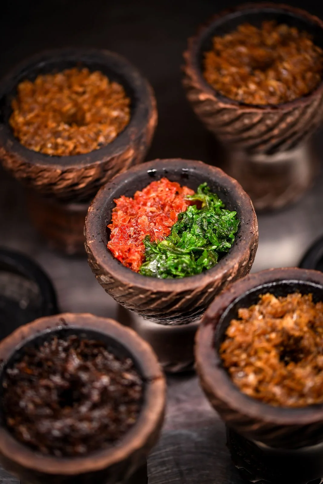 Clay hookah bowls filled with tobacco in different colors, red and green tobacco in the middle one