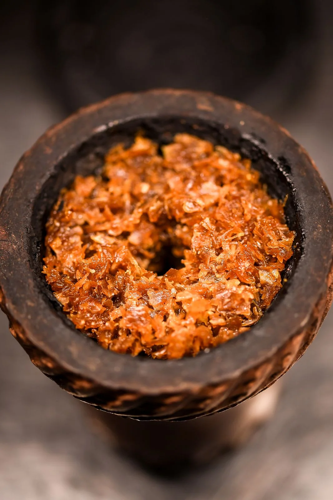 Clay hookah bowl filled with orange tobacco leaves, top view