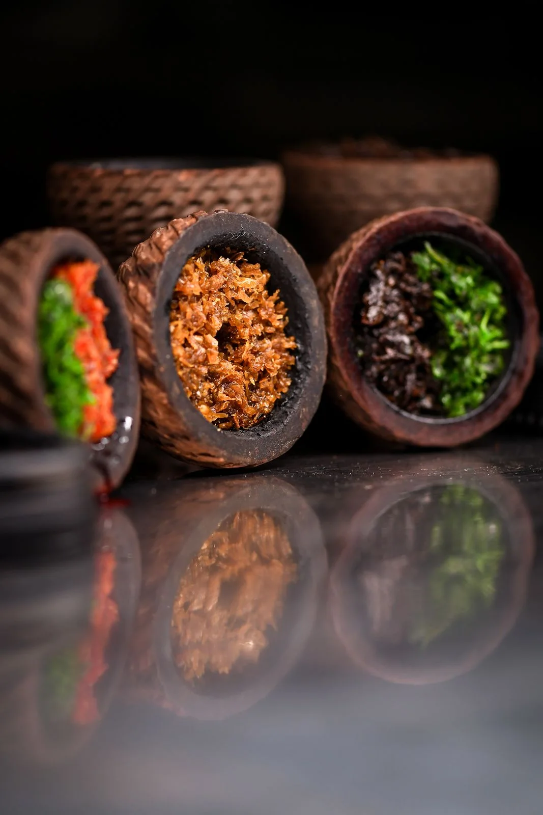 Clay hookah bowls with tobacco set on a glossy dark surface, with their reflection