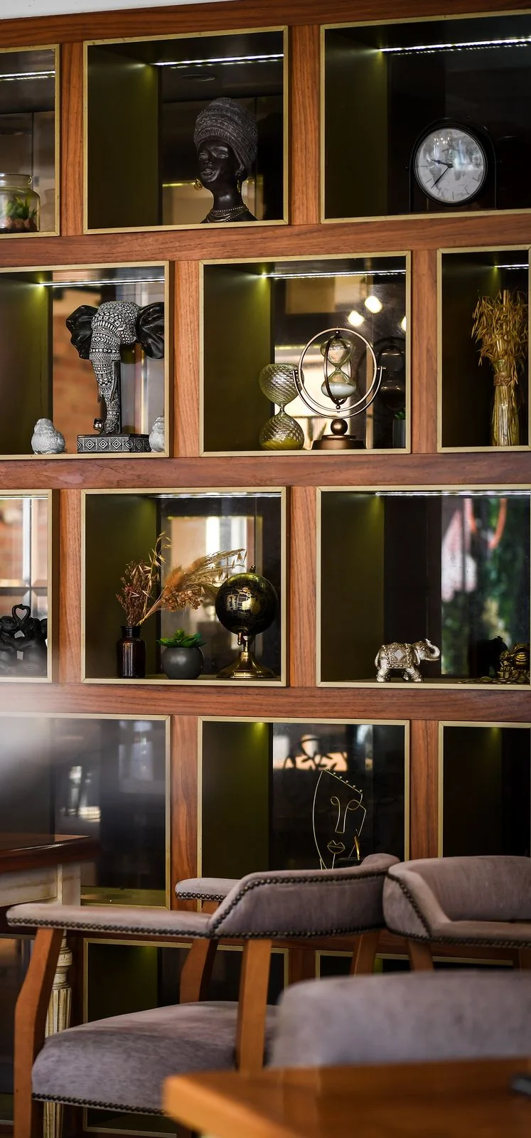 Wooden shelves with lit niches: a globe, an hourglass, a table clock and elephant figurines, armchairs in front