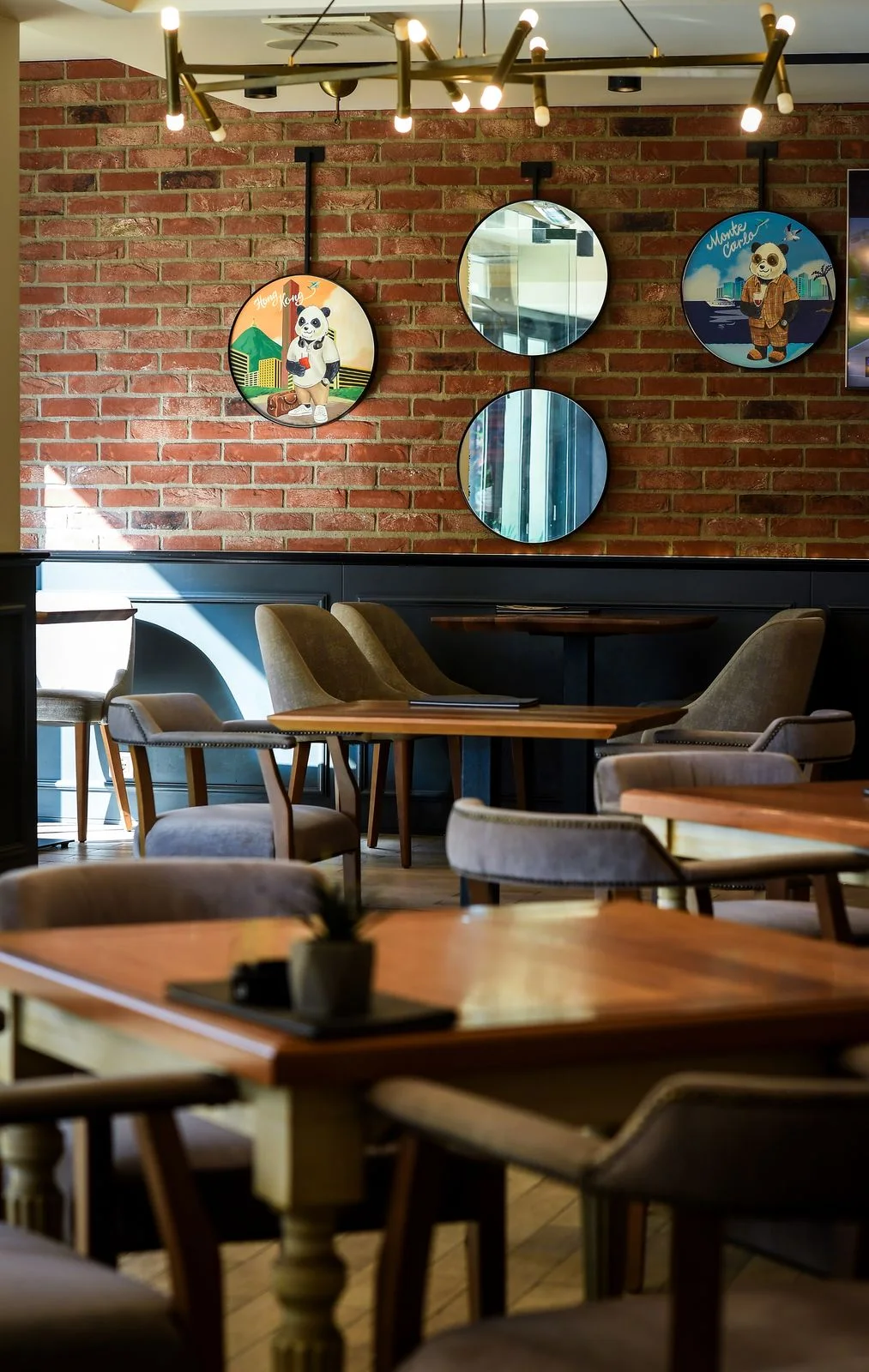 Brick wall with panda paintings and round mirrors, a gold chandelier, wooden tables and armchairs