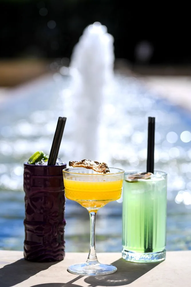 Cocktails in the garden with a fountain: a purple tiki mug, a yellow and a green cocktail in the sun
